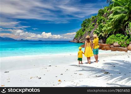 Family on beautiful Petite Anse beach, young couple in yellow with three year old toddler boy. Summer vacation at Seychelles, Mahe.