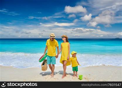 Family on beautiful Petite Anse beach, young couple in yellow with three year old toddler boy. Summer vacation at Seychelles, Mahe.