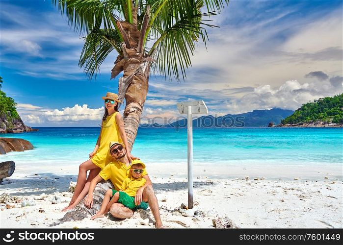 Family on beautiful Petite Anse beach, young couple with three year old toddler boy sitting on palm tree. Summer vacation at Seychelles, Mahe.