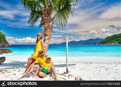 Family on beautiful Petite Anse beach, young couple with three year old toddler boy sitting on palm tree. Summer vacation at Seychelles, Mahe.