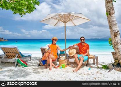 Family on beautiful Petite Anse beach, young couple with three year old toddler boy sitting on sun bed. Summer vacation at Seychelles, Mahe.