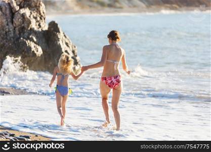 Family on the beach on sunset. Mother and daughter runing together.