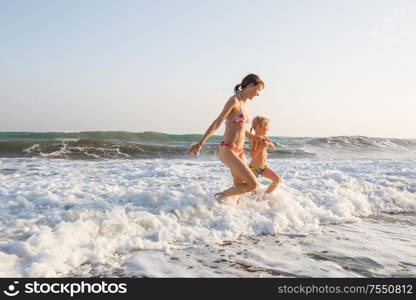 Family on the beach on sunset. Mother and daughter running together.