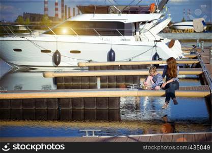 Family on vacation - mother and daughter are sitting on the pier on the background of yachts. Ukraine