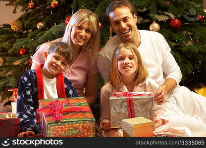 Family Opening Christmas Present In Front Of Tree