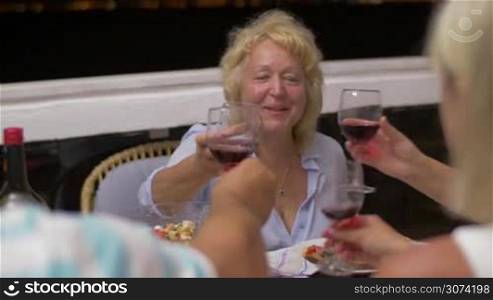 Family or group of friends having meal on outdoor balcony late in the evening. People toasting, focus on senior cheerful woman drinking red wine