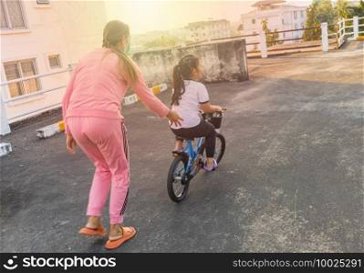 family outdoor activity. Asian Mother teaching child to ride a bike at the field in the morning.