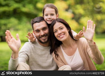 family, parenthood, adoption and people concept - happy mother, father and little girl in summer park waving hands