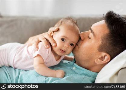 family, parenthood and fatherhood concept - middle aged father kissing little baby daughter lying on sofa at home. middle aged father kissing baby daughter at home