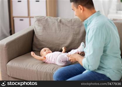family, parenthood and fatherhood concept - middle aged father playing with little baby daughter lying on sofa at home. middle aged father playing with baby at home