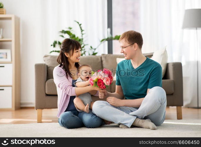 family, parenthood and mothers day concept - happy mother receiving flower bunch from father and baby boy at home. happy family with flowers and baby boy at home