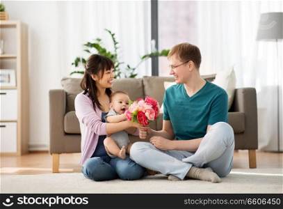 family, parenthood and mothers day concept - happy mother receiving flower bunch from father and baby boy at home. happy family with flowers and baby boy at home