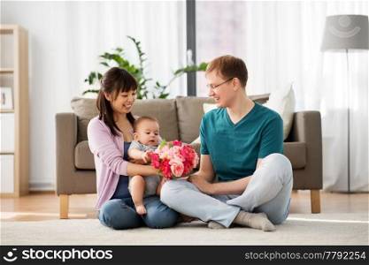 family, parenthood and mothers day concept - happy mother receiving flower bunch from father and baby boy at home. happy family with flowers and baby boy at home