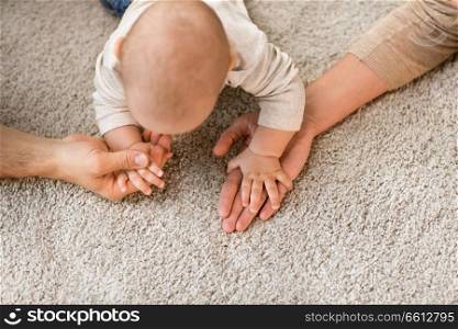 family, parenthood and people concept - close up of baby holding to mother and father hands on carpet. close up of family with baby on carpet