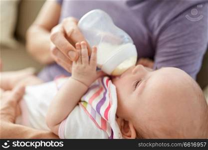 family, parenthood and people concept - close up of father feeding little daughter with baby formula from bottle at home. close up of father feeding baby from bottle