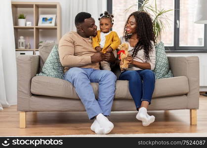 family, parenthood and people concept - happy african american mother and father with baby daughter sitting on sofa at home. happy african family with baby daughter at home