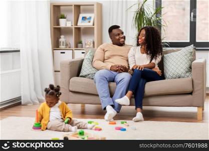 family, parenthood and people concept - happy african american mother and father looking at baby daughter playing with toy blocks at home. african family with baby daughter playing at home