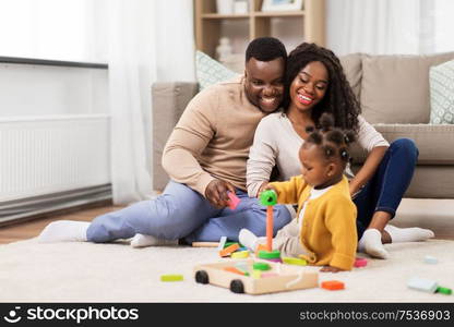 family, parenthood and people concept - happy african american mother, father and baby daughter playing with toy blocks at home. african family playing with baby daughter at home