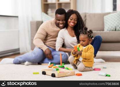 family, parenthood and people concept - happy african american mother, father and baby daughter playing with toy blocks at home. african family playing with baby daughter at home