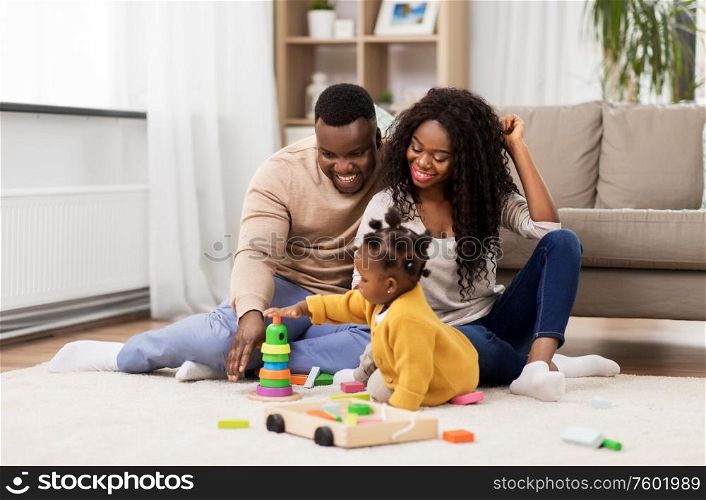 family, parenthood and people concept - happy african american mother, father and baby daughter playing with toy blocks at home. african family playing with baby daughter at home