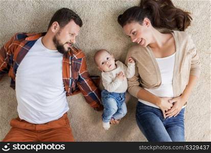 family, parenthood and people concept - happy mother and father with baby lying on floor at home. happy family with baby lying on floor at home