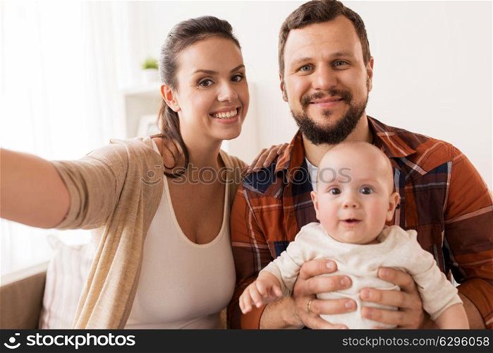 family, parenthood and people concept - happy mother and father with baby taking selfie at home. mother and father with baby taking selfie at home
