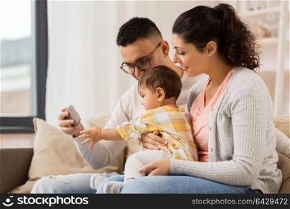family, parenthood and people concept - happy mother, father and baby daughter with smartphone at home. mother, father and baby with smartphone at home