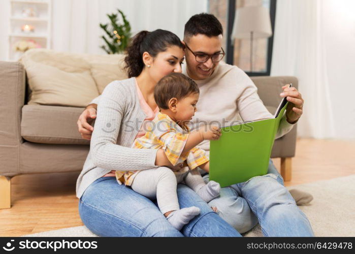 family, parenthood and people concept - happy mother, father and baby daugter reading book at home. happy family with baby reading book at home