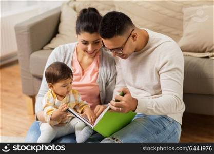 family, parenthood and people concept - happy mother, father and baby daugter reading book at home. happy family with baby reading book at home