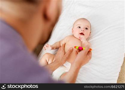 family, parenthood and teething concept - happy father and little baby daughter with rattle toy at home. close up of father and baby with rattle toy