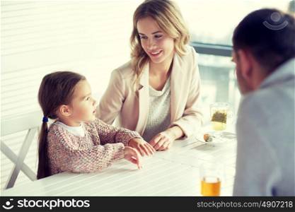 family, parenthood, communication and people concept - happy mother, father and little girl having dinner and talking at restaurant or cafe. happy family having dinner at restaurant or cafe