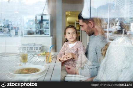 family, parenthood, communication and people concept - happy mother, father and little girl having dinner and talking at restaurant or cafe