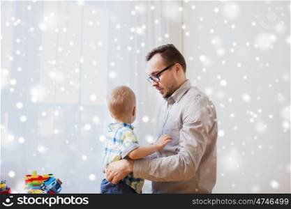 family, parenthood, fatherhood nd people concept - father taking care of little son at home over snow