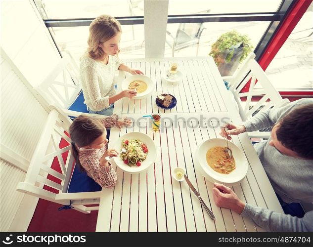 family, parenthood, food and people concept - happy mother, father and little girl eating soup and pasta for dinner at restaurant or cafe