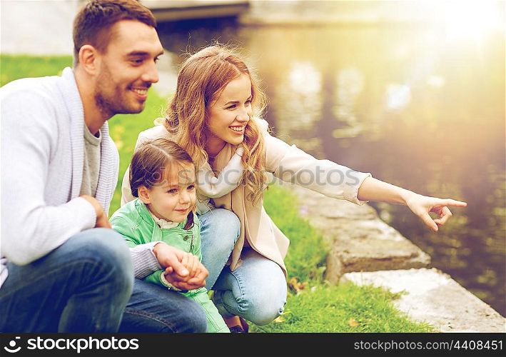 family, parenthood, leisure and people concept - happy mother, father and little girl walking in summer park near pond