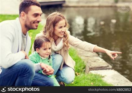 family, parenthood, leisure and people concept - happy mother, father and little girl walking in summer park near pond