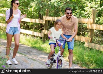 family, parenthood, leisure and people concept - happy mother, father and little daughter learning to ride bicycle in summer park. kid with patents learning to ride bicycle in park