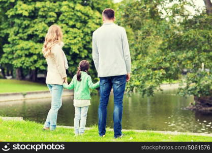family, parenthood, leisure and people concept - mother, father and little girl walking in summer park near pond. family walking in summer park