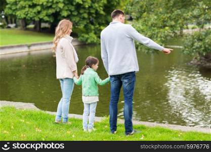 family, parenthood, leisure and people concept - mother, father and little girl walking in summer park near pond