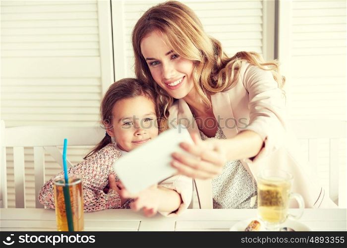 family, parenthood, technology and people concept - happy mother and little girl having dinner and taking selfie by smartphone at restaurant