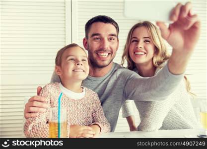 family, parenthood, technology and people concept - happy mother, father and little girl having dinner and taking selfie by smartphone at restaurant. happy family taking selfie at restaurant