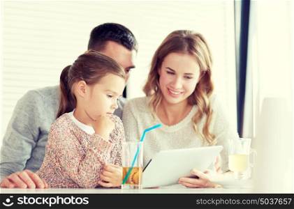 family, parenthood, technology and people concept - happy mother, father and little girl with tablet pc computer having dinner at restaurant. happy family with tablet pc at restaurant