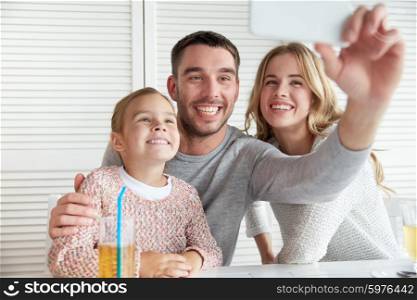 family, parenthood, technology and people concept - happy mother, father and little girl having dinner and taking selfie by smartphone at restaurant