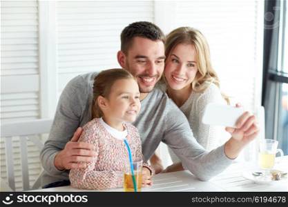 family, parenthood, technology and people concept - happy mother, father and little girl having dinner and taking selfie by smartphone at restaurant