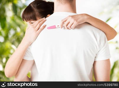 family, parenting and medical concept - woman with pregnancy test hugging man