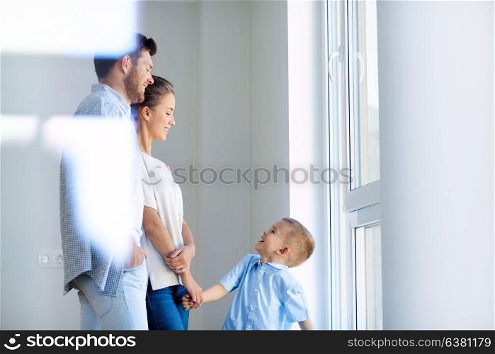 family, people and real estate concept - happy mother, father and little son at window in new home or apartment. happy family with child at new home or apartment