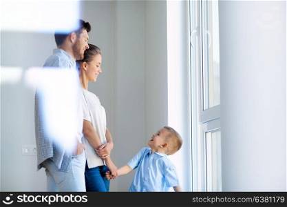 family, people and real estate concept - happy mother, father and little son at window in new home or apartment. happy family with child at new home or apartment