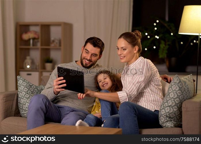 family, people and technology concept - happy smiling father, mother and little daughter with tablet pc computer at home at night. happy family with tablet computer at home at night