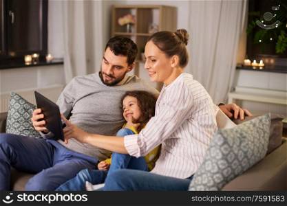 family, people and technology concept - happy smiling father, mother and little daughter with tablet pc computer at home at night. happy family with tablet computer at home at night