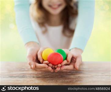 family, people, holiday and childhood concept - close up of happy girl and mother hands holding colored eggs